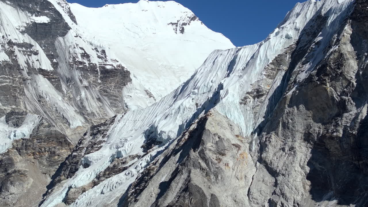 La telecamera cinematografica si inclina verso l'alto, rivelando l'Island Peak nella regione dell'Everest in Nepal, mostrando le imponenti montagne dell'Himalaya sotto un cielo alpino limpido.