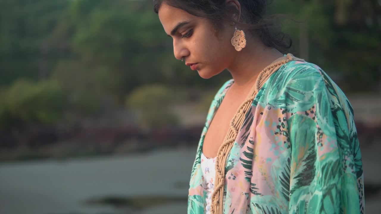 Portrait of a beautiful young woman looking at the ocean, on a sandy tropical beach, at dusk