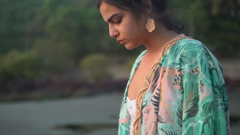 Portrait-of-a-beautiful-young-woman-looking-at-the-ocean,-on-a-sandy-tropical-beach,-at-dusk