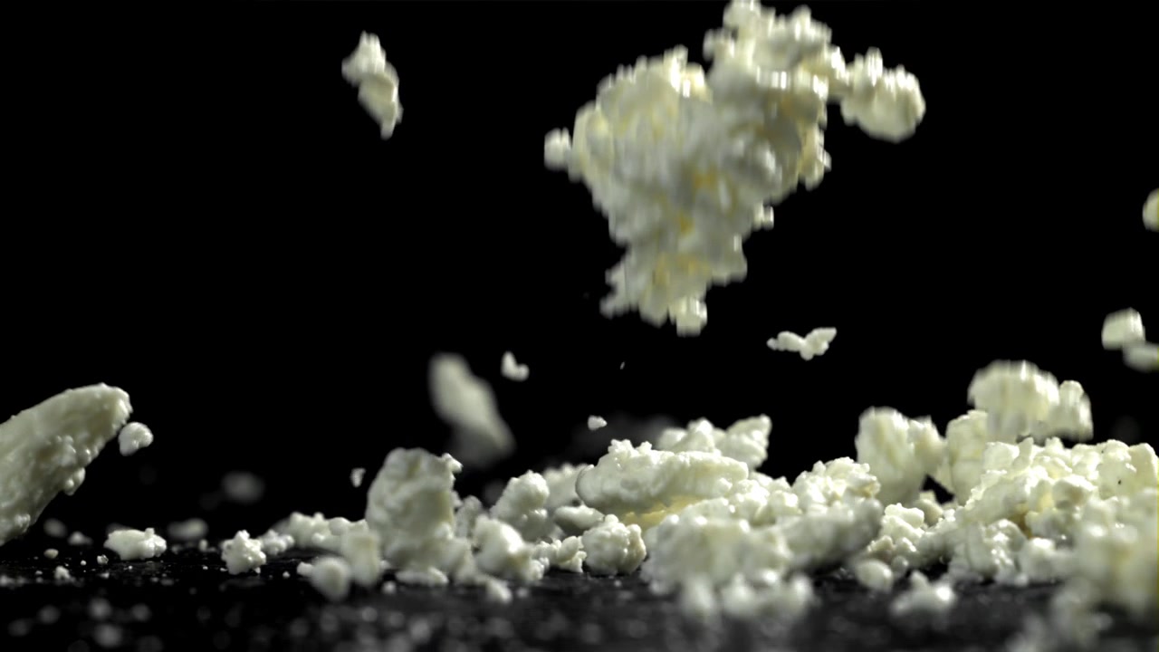 Fersk cottage cheese faller i sakte film på svart bakgrunn