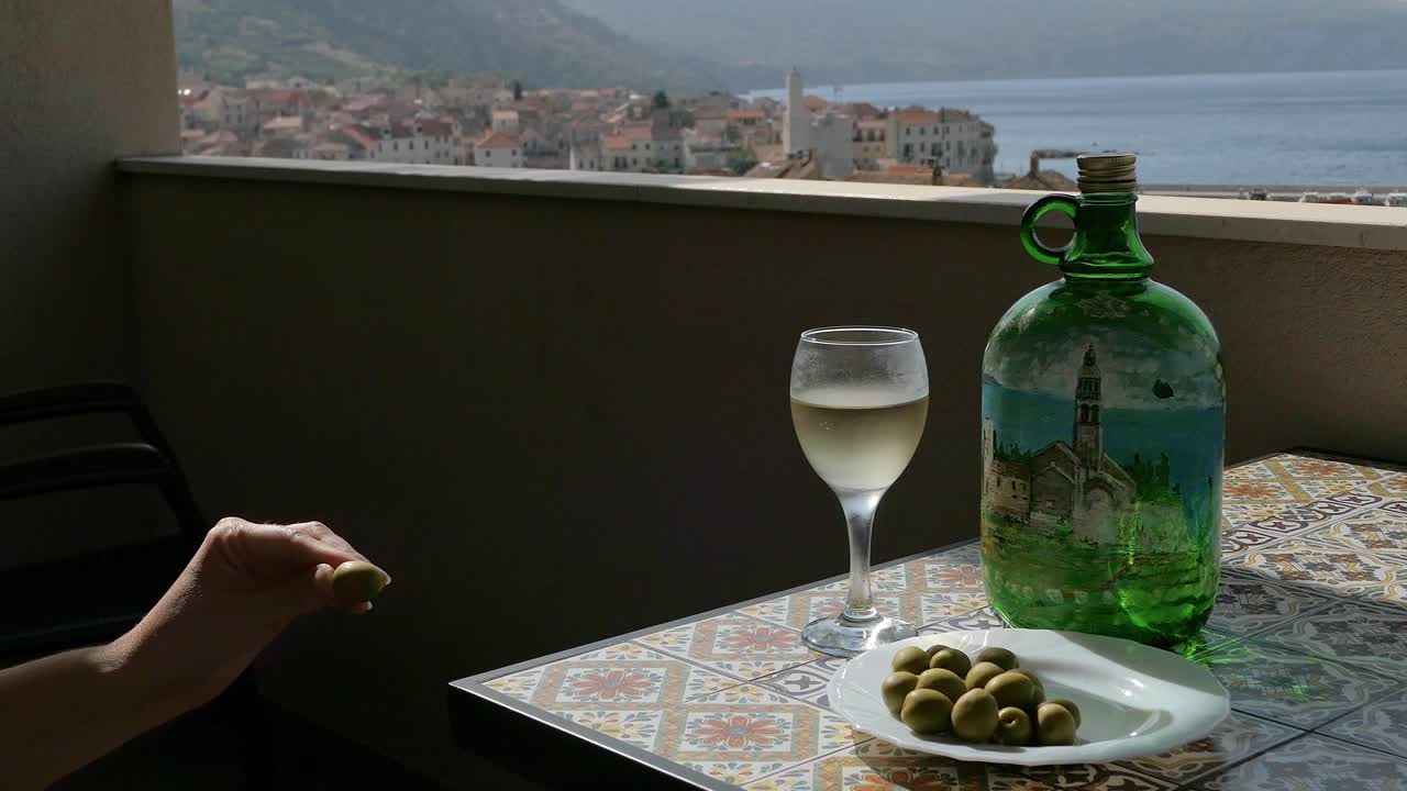 mujer disfrutando de aceitunas verdes con vino en la terraza de una ciudad costera