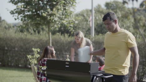 man standing at barbeque grill and blowing up fire with lid