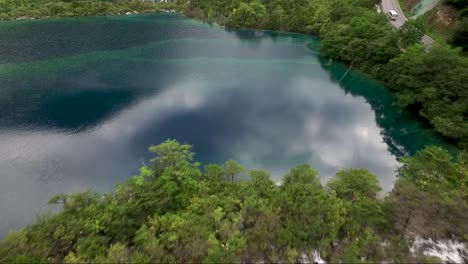 reversal drone shot over dark blue water and past a tree line with multiple small waterfalls