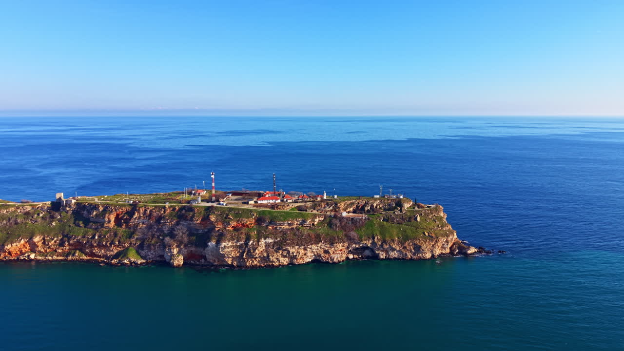 Vista di una scogliera costiera con un faro circondato da acqua blu e cielo sereno nel pomeriggio