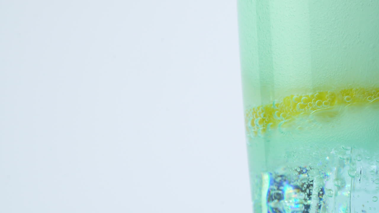 Fizzy soda drink pouring into glass with ice and lemon slice close up shot