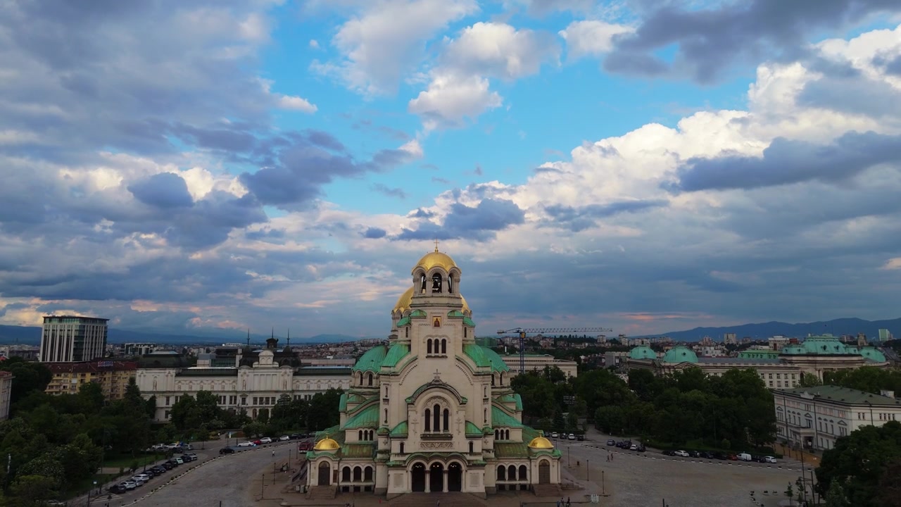 Plano aéreo de seguimiento medio hacia atrás que revela la majestuosa estructura de la Catedral de Alexander Nevsky bajo un cielo nublado dramático en Sofía, capital de Bulgaria