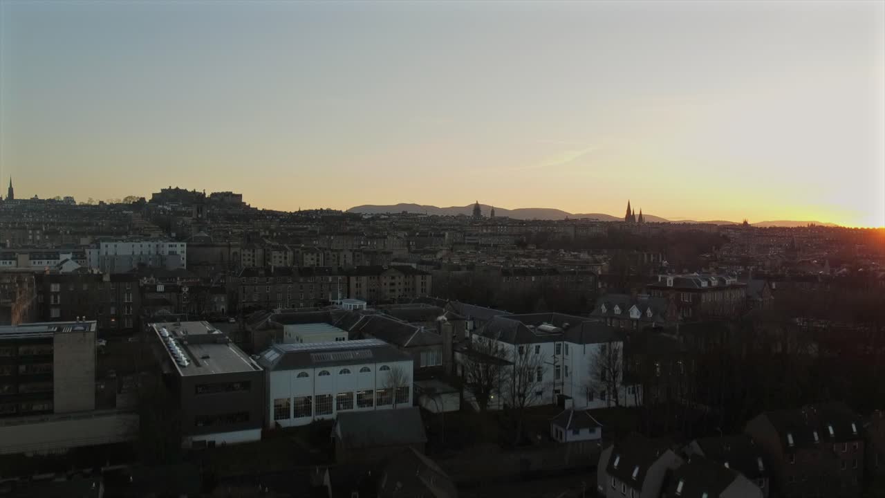 Evening cityscape of Edinburgh during sunset, showcasing historic buildings and the distant skyline. The fading light casts soft shadows over the urban architecture and the horizon.