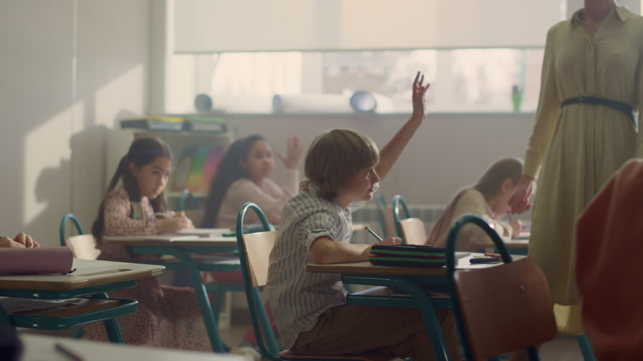 Kids sitting at desks in school class. Teacher checking home work in classroom