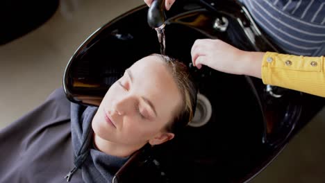 Hands-of-caucasian-female-hairdresser-washing-hair-of-relaxed-female-customer-at-hair-salon