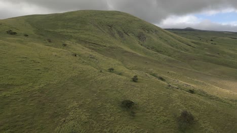 aerial rises over barren green meadow on rolling volcanic hawaii hills