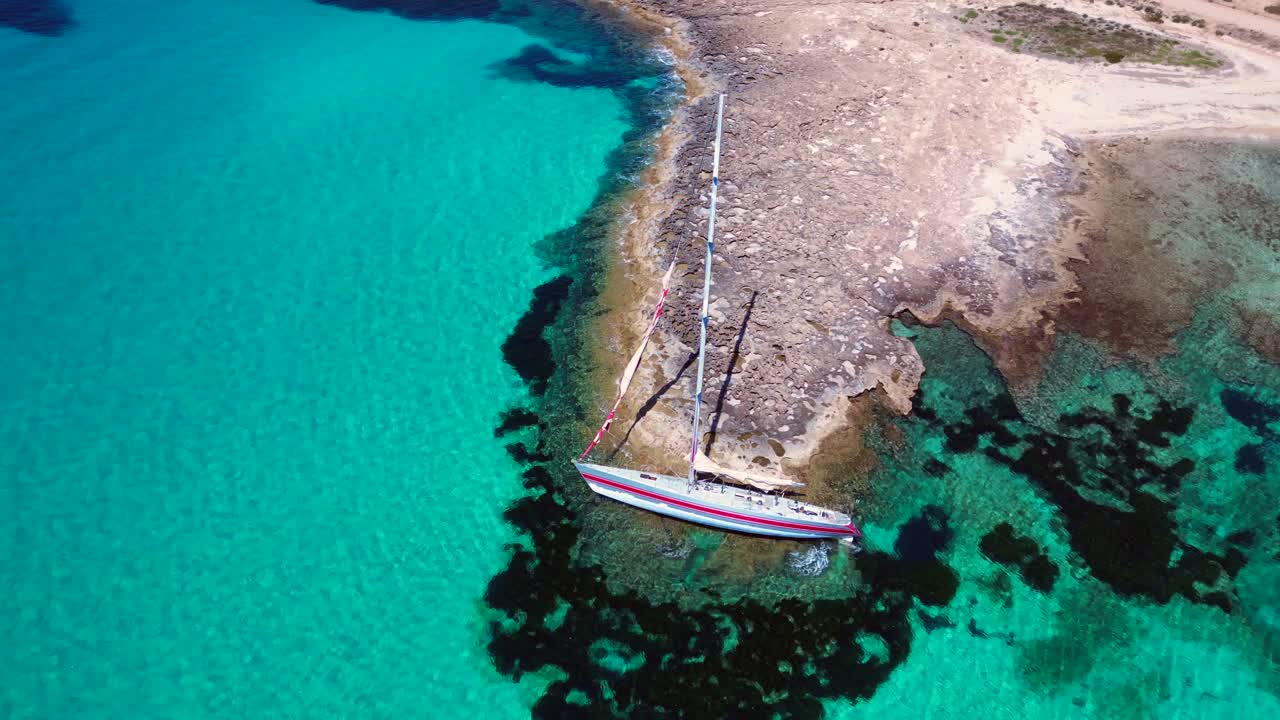 Sailboat stranded on cliff near the coast of Formentera Island, Spain, during a summer sunny day. Great aerial view flight circle drone footage