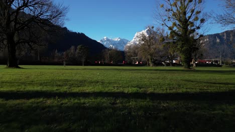 Toma-Aérea-De-Campo-Verde-Con-Hermoso-Paisaje-De-Los-Alpes-Suizos-Al-Fondo-En-Walensee,-Suiza