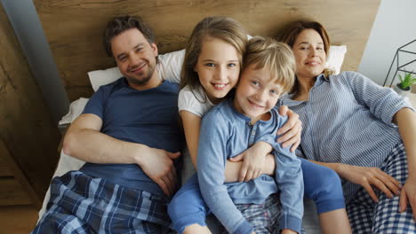 vista superior de niños lindos sentados en la cama entre sus padres jóvenes que están mintiendo