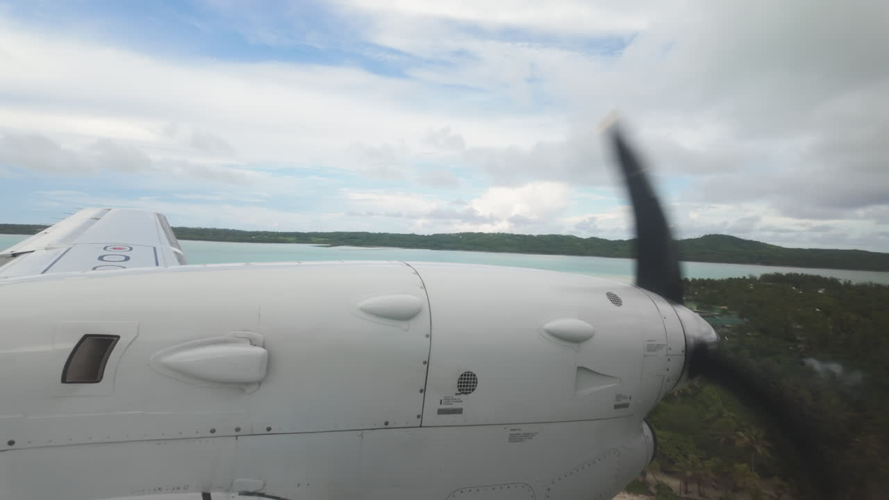 Plane approaches in slow motion view from inside airplane looking out at wing and propellor over tropical islands