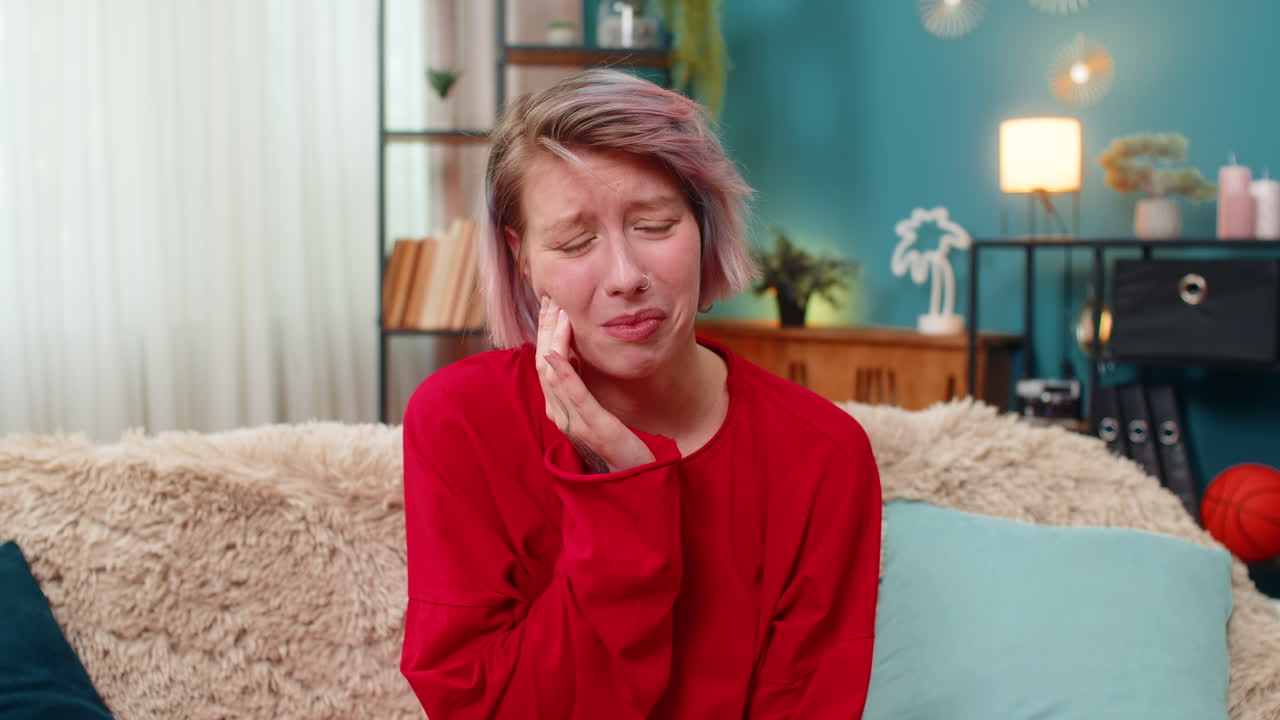 Young woman holding cheek experiencing toothache pain painful uncomfortable facial expression home