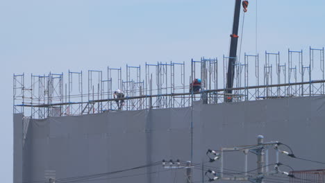 Construction-Workers-Working-On-Scaffoldings-In-A-Building-Project-With-Crane-On-A-Hot-Weather