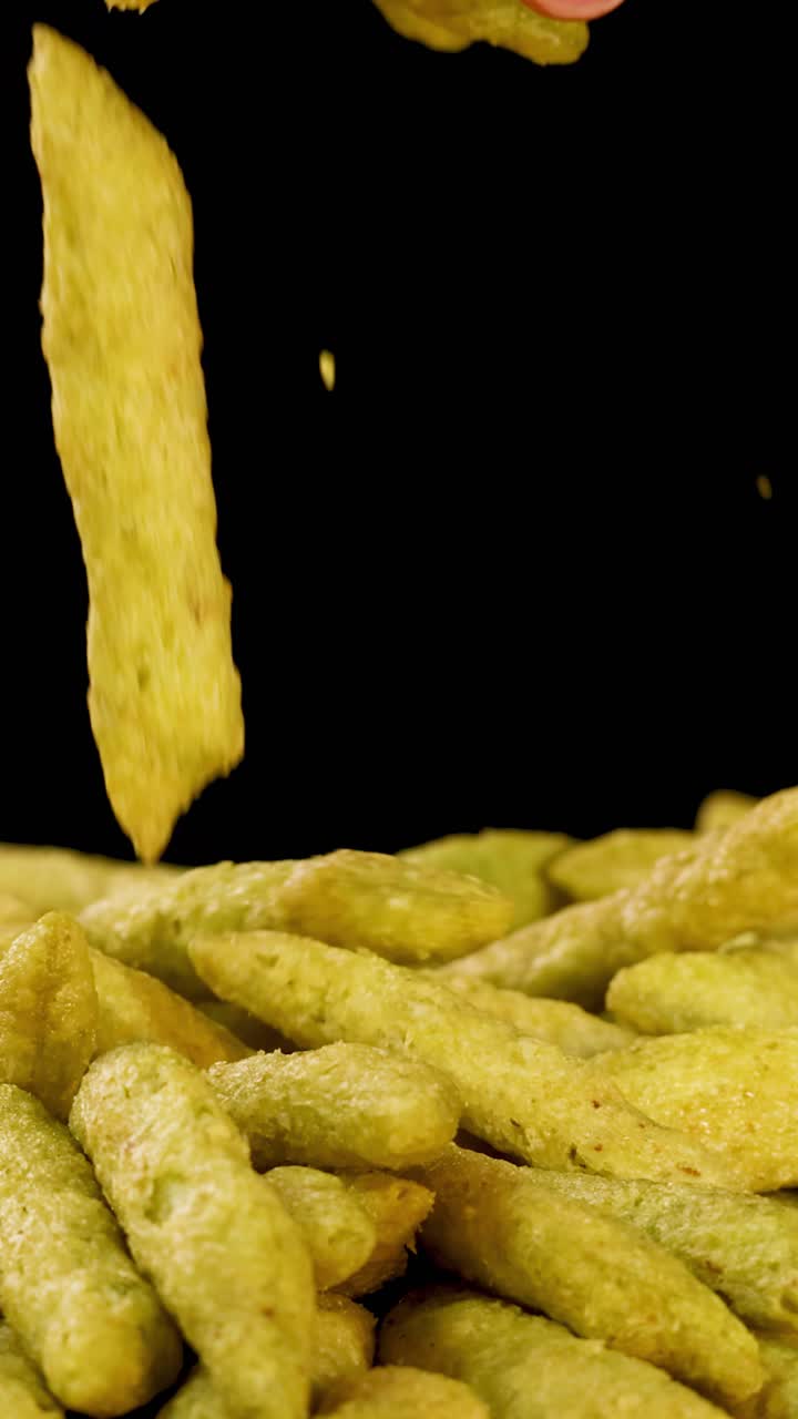 Mano umana seleziona snack soffiati ai piselli verdi da un mucchio, primo piano, sfondo nero, illuminazione brillante.