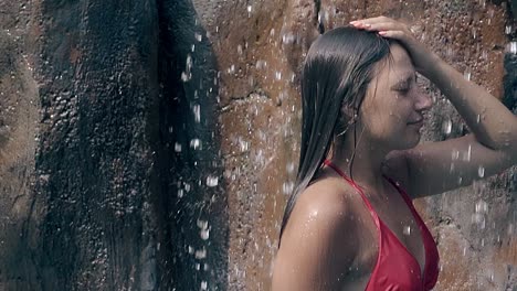 lady in red bikini under waterfall at stones slow motion