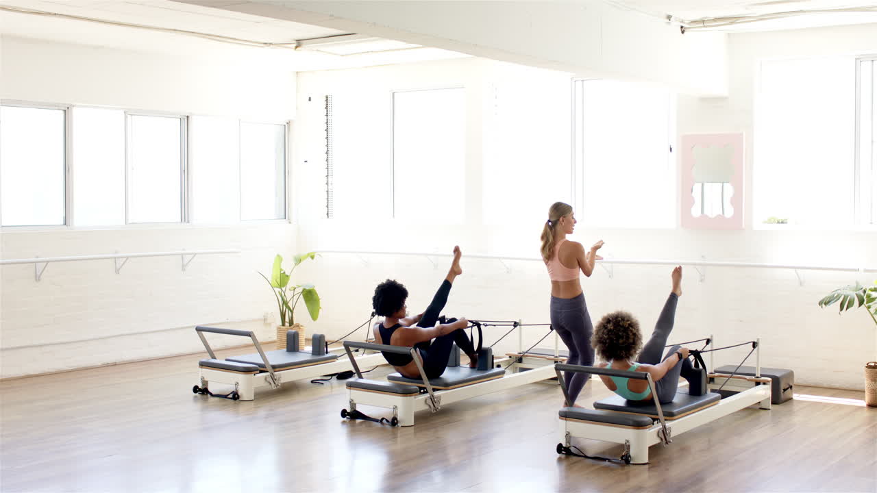 tres mujeres están haciendo ejercicio en máquinas reformadoras de pilates en un estudio brillante