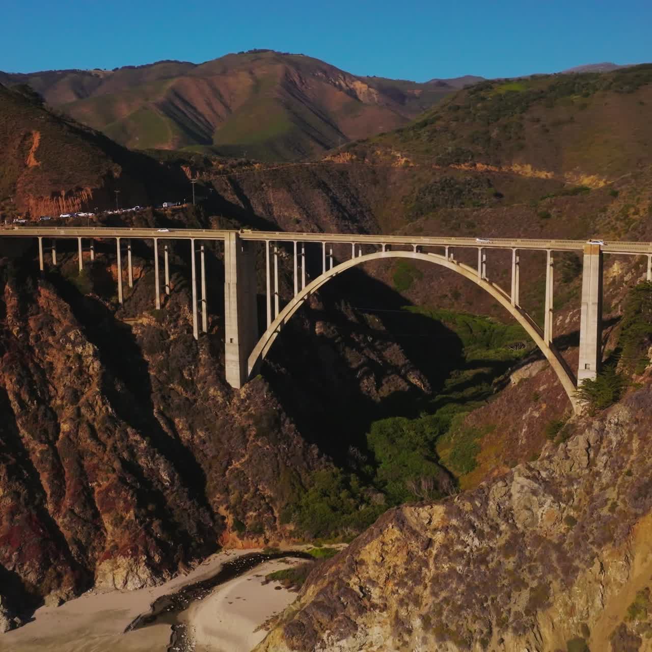 Arched bridge over the gap between the mountains. Sunlit mountains of California in the bright rays of sun. Aerial perspective
