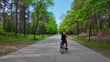 man cycling on a scenic road through a lush green forest