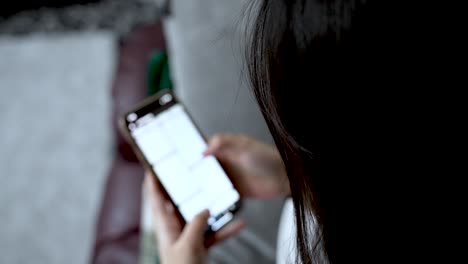 over shoulder view of a woman holding a smartphone, scrolling through the screen while engaging with social media and browsing online content