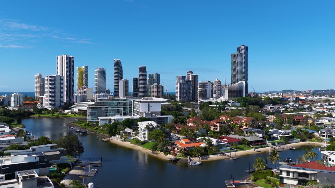 Aerial footage captures the Gold Coast skyline with high-rise buildings and waterways under clear blue skies