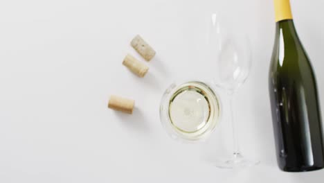 white wine bottle, glasses and cork lying on white surface with copy space