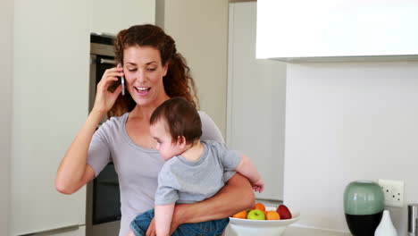 Mother-holding-her-happy-baby-boy-and-talking-on-phone