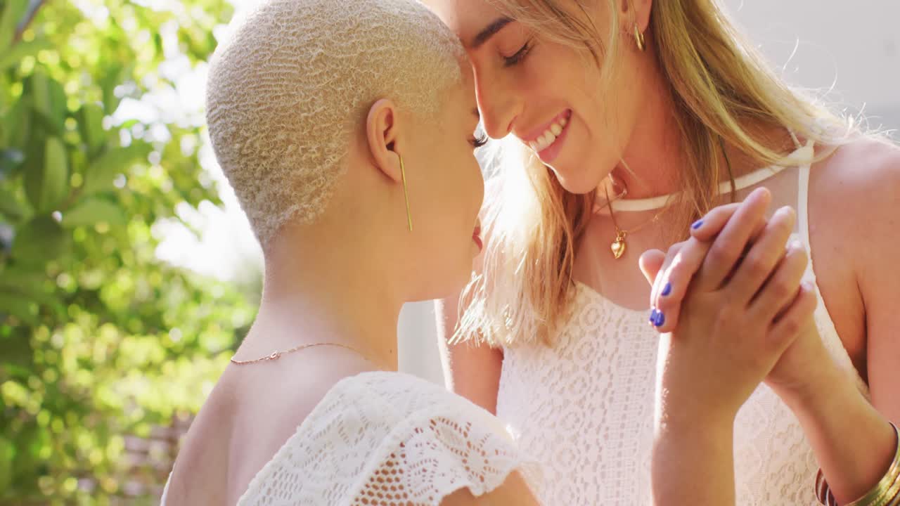 feliz pareja de mujeres diversas cogidas de las manos y bailando en el jardín