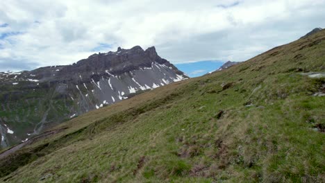 imágenes aéreas de drones que vuelan lento y bajo sobre una ruta de senderismo que conduce a lo largo de laderas cubiertas de hierba hacia una espectacular cresta montañosa irregular con parches residuales de nieve