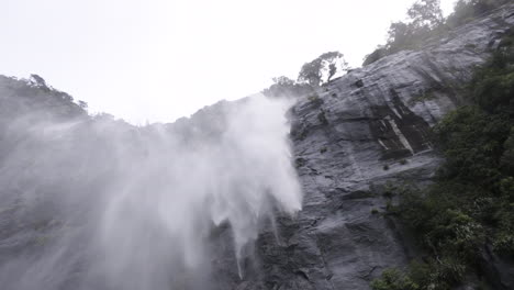 toma en cámara lenta de una cascada que se estrella contra un acantilado y se la lleva el viento
