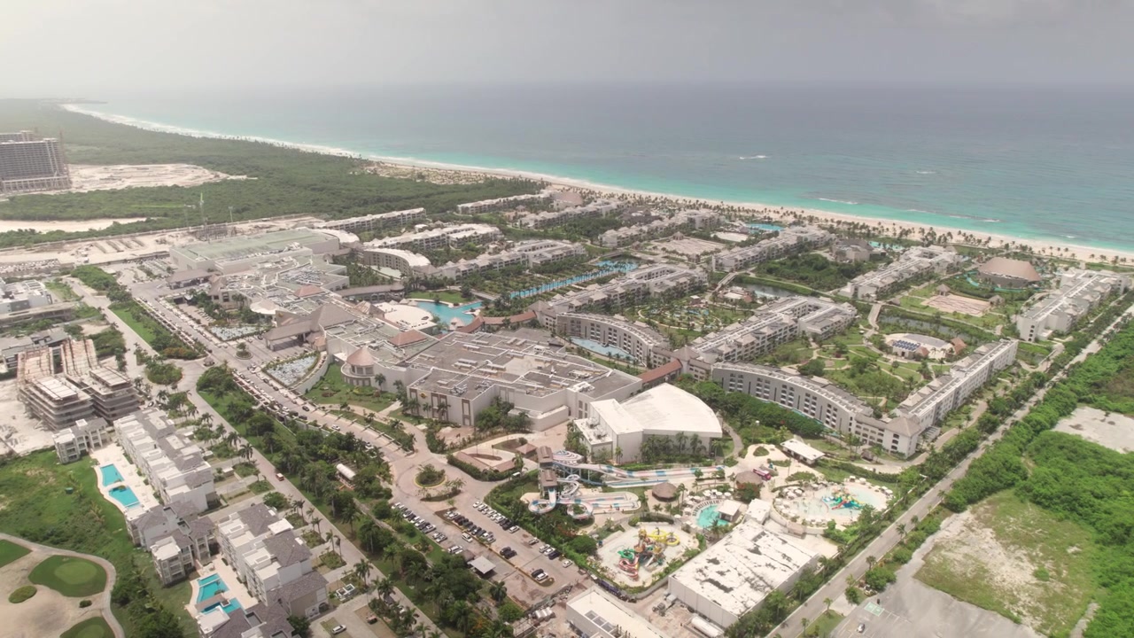 Punta Cana'da, lüks altyapı, golf sahası yeşillikleri ve Karayip plaj manzaraları içeren geniş bir sahil tatil köyü topluluğunun yüksek açılı hava drone taraması.