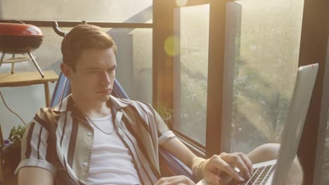 caucasian man browsing on laptop computer while relaxing on a hammock at home