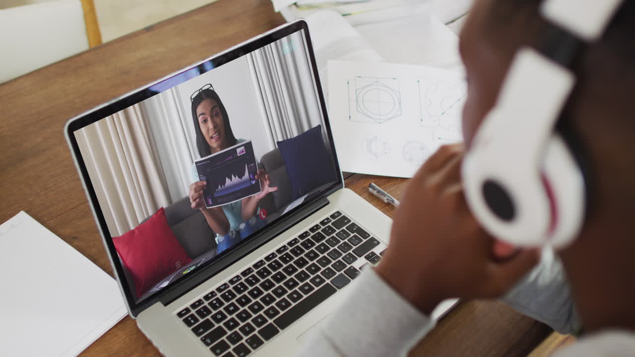 African american male college student wearing headphones having a video call on laptop at home