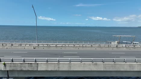 Vista-Lateral-Del-Dron-En-Una-Toma-De-Seguimiento-Del-Puente-Conmemorativo-Ted-Smout,-Cámara-Sobre-El-Agua-En-La-Bahía-De-Moreton-Con-El-Océano-Abierto-De-Fondo,-Tomada-Al-Mediodía-En-Un-Día-Claro-Y-Soleado