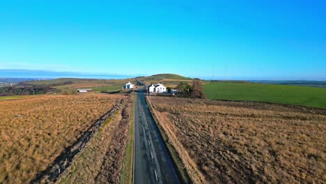 Aerial-drone-video-footage-moving-slowly-down-a-country-road-and-passing-white-washed-buildings,-high-on-the-Pennine-Hills,-UK