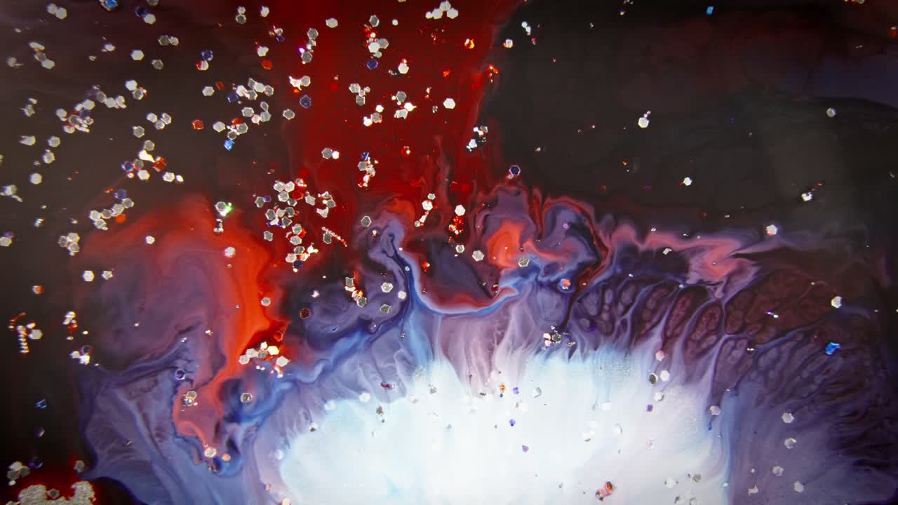 Red and blue ink merging in water with sparkling particles, creating a dynamic and abstract fluid art scene