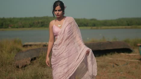 Frau-In-Rosa-Saree-Am-Fluss-Mit-Boot,-üppiges-Grün-Im-Hintergrund,-Ruhige-Und-Kulturelle-Stimmung