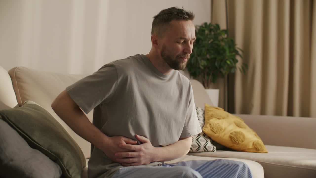 Uomo che soffre di mal di stomaco mentre è seduto sul divano a casa.