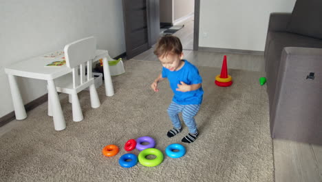 lovely caucasian kid puts the rings from toy pyramid in the pile. joyful toddler jumping and clapping happily. high angle view.