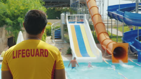 rear view - the rescuer watches people on the water slides working in the water park