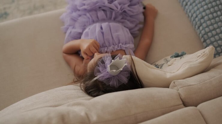 Young girl sitting comfortably on a sofa in a cozy home setting, looking calm and relaxed. Perfect for themes of childhood, home life, relaxation, and family moments.