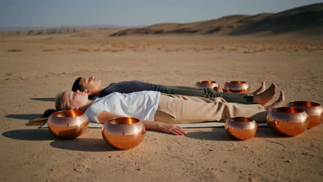 two people meditating with singing bowls in a desert landscape