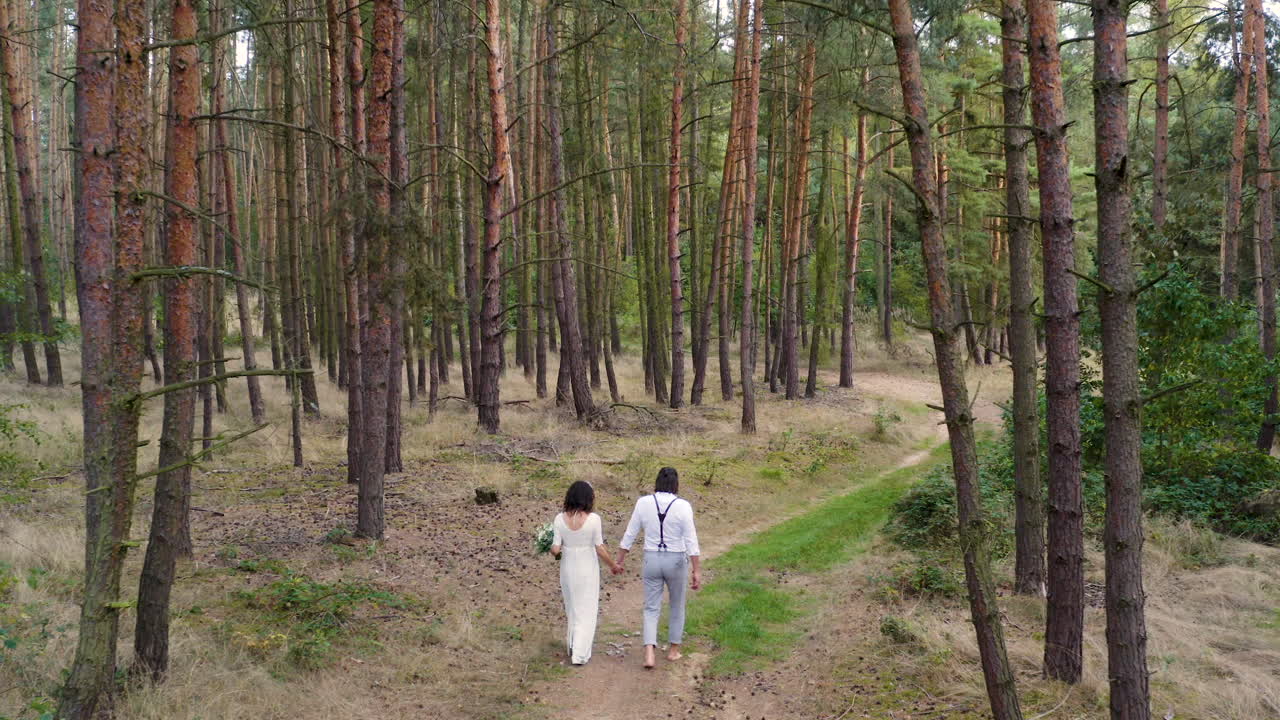 Coppia di novelli sposi che cammina a piedi nudi su una strada forestale, lanciando il bouquet