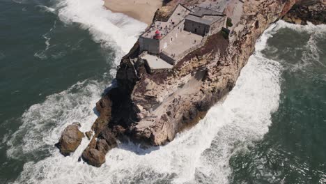 ocean waves crashing on nazaré lighthouse cliff, portugal