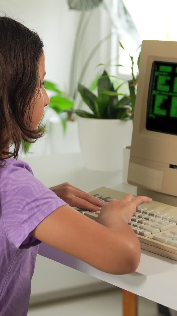 A young girl types on a retro computer in a bright, modern room. The vertical video captures the nostalgic feel of the vintage tech and the serene ambiance with lush plants