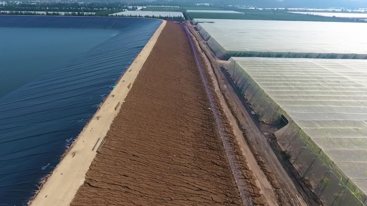 Aerial tilt down to show the side of a solar collection array and the dark rubber covering, bank and surroundings.