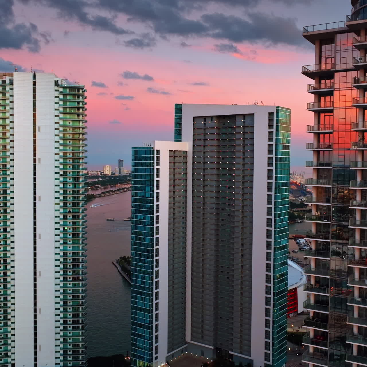 Approaching beautiful high-rise buildings with glass windows reflecting setting sun. Miami, Florida, USA. Lovely pink-blue sky at backdrop.