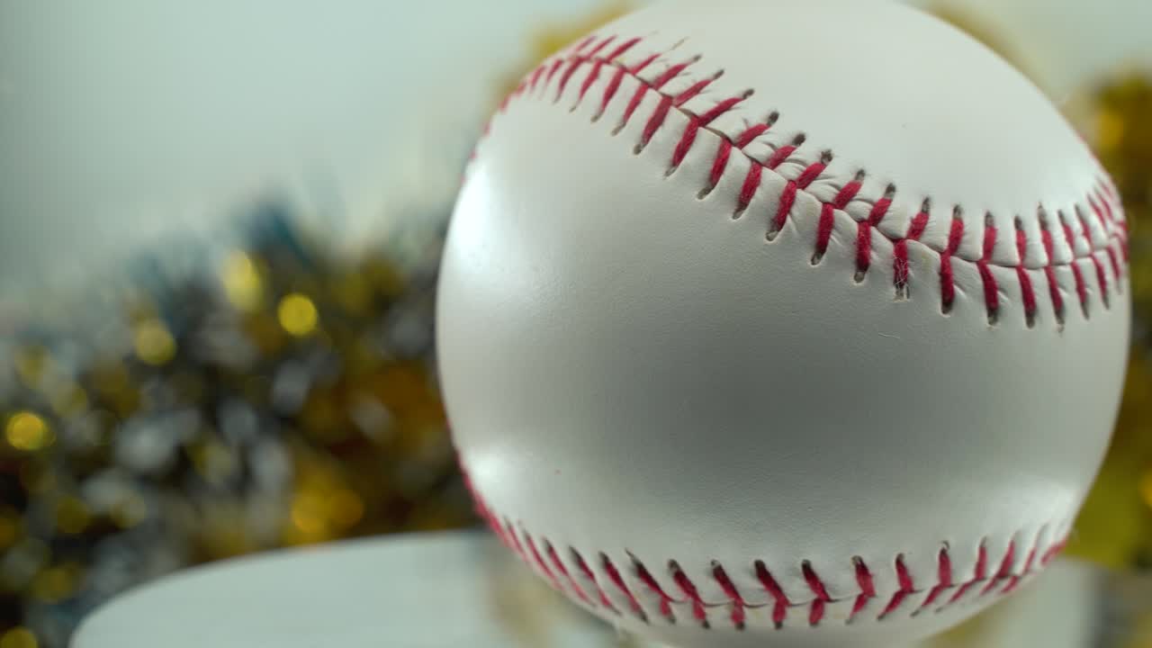 toma cinematográfica de primer plano de una pelota de base blanca, puntos rojos de béisbol en un soporte brillante, decoraciones de navidad borrosas en el fondo, iluminación de estudio profesional, panela de video 4k a la derecha